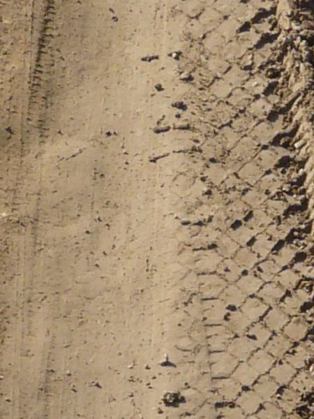 Dirt road texture in brown tone with metal mesh in surface and tire marks.